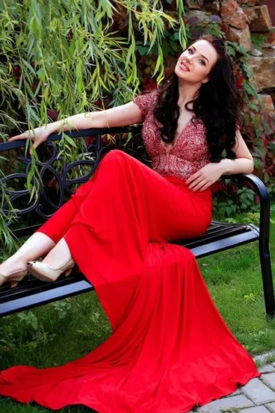 Iris is seated in a red gown, legs crossed, relaxed