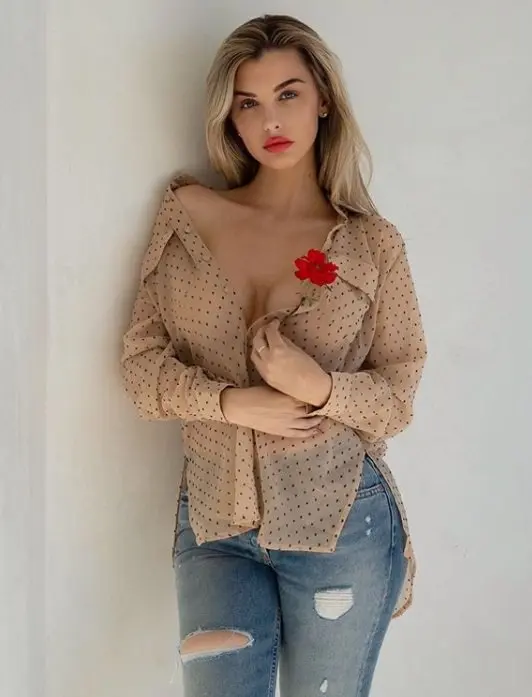 De blonde escort Emilia in een beige trui, met een roos in haar hand